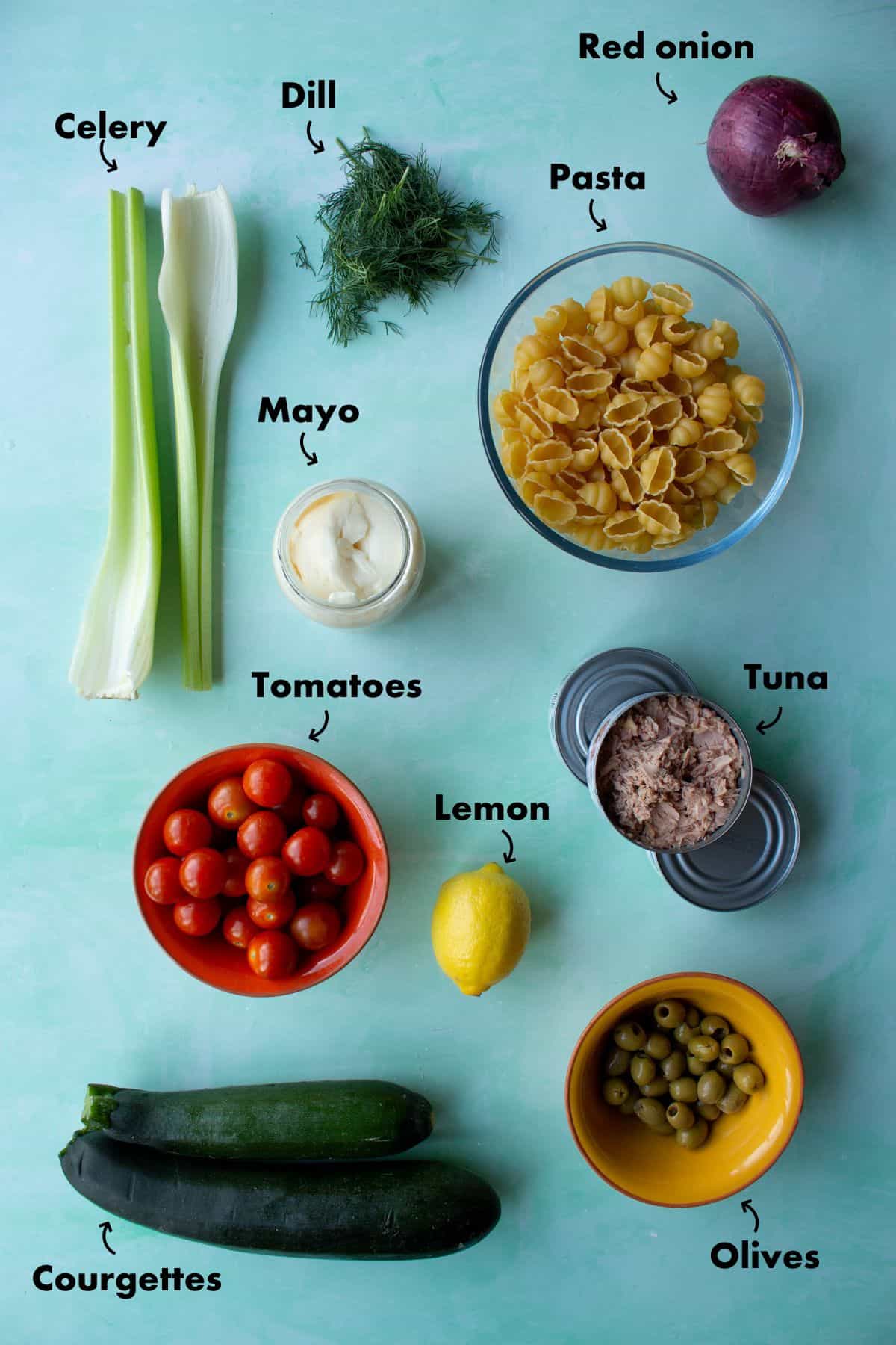 Ingredients to make Tuna Pasta salad laid out on a blue background and labelled.
