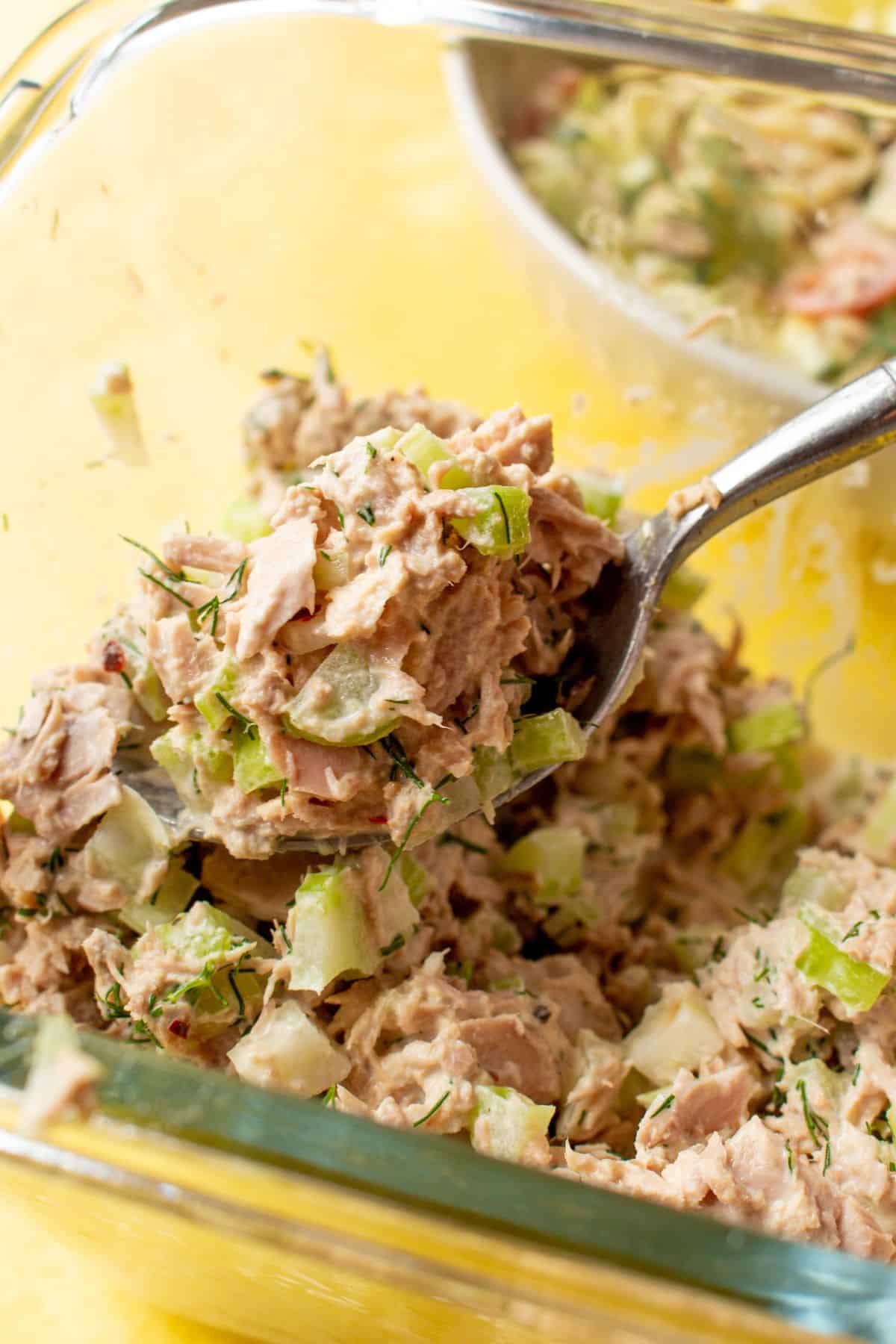 Tuna mayo mixed with chopped celery in glass bowl with spoon.