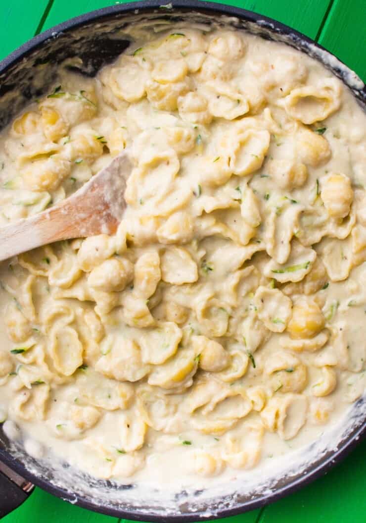 Close up of Cauliflower Alfredo Pasta with Courgette with a wooden spoon on a green background.