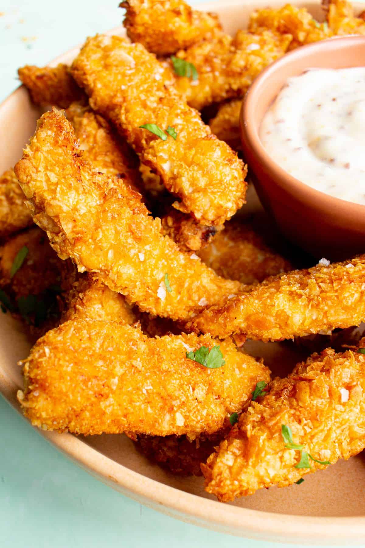 Close up shot of Chicken Goujons baked with cornflakes with some dipping sauce.