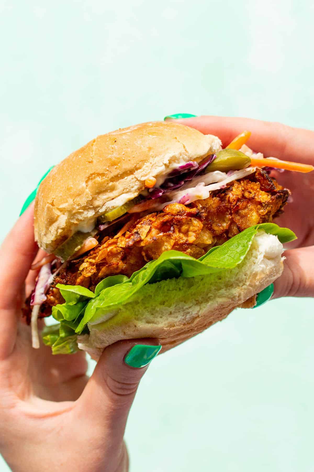 Spicy chicken sandwich side shot with hands holding the bun filled with lettuce, large piece of chicken and coleslaw.