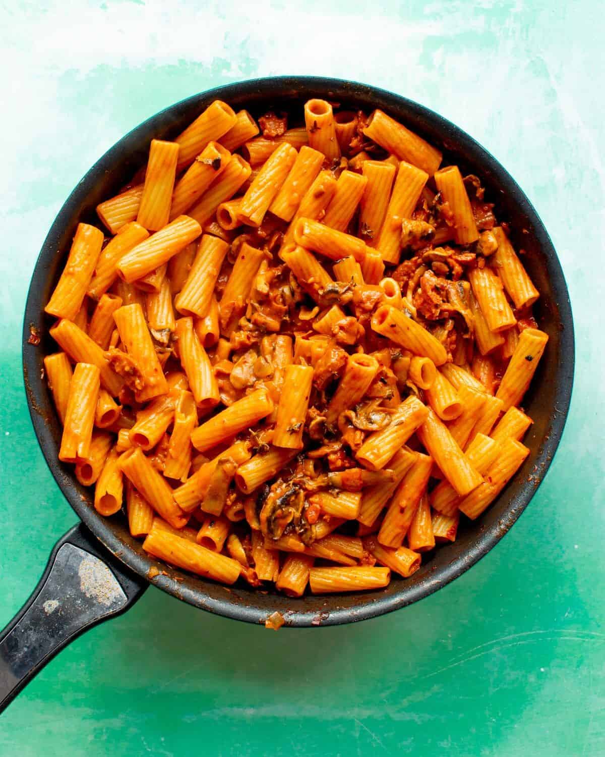 Creamy Chorizo pasta ready to serve in large pan on a green back ground.