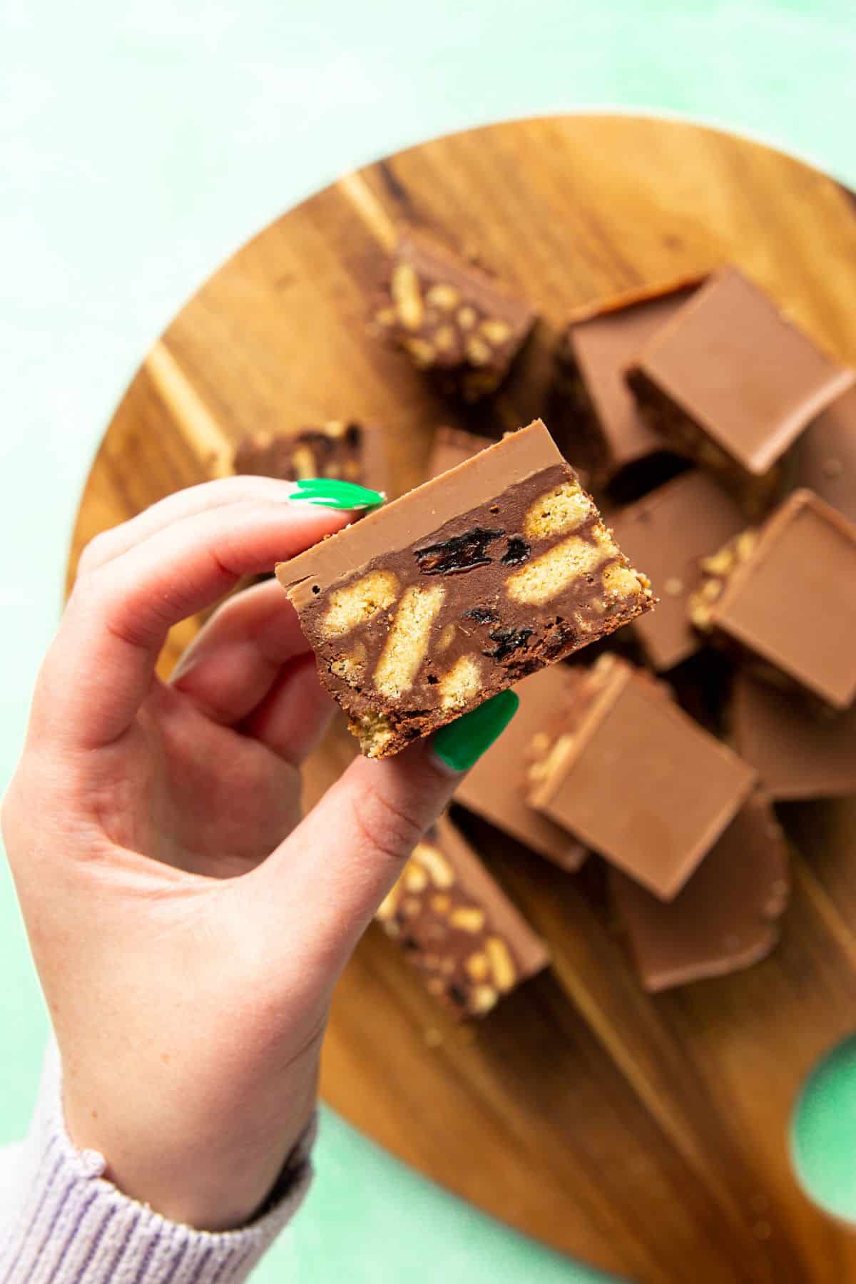 A piece of Tiffin cake being held above lots of pieces of Tiffin cake on a board.