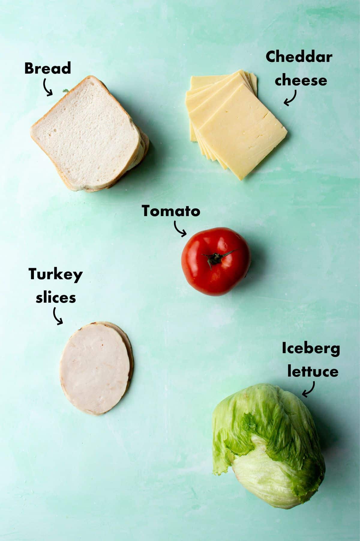 Ingredients to make turkey sandwich, sliced white bread, turkey slices, lettuce, tomato and cheddar cheese slices.
