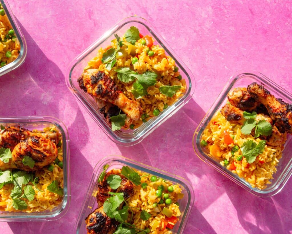 Peri Peri chicken drumsticks with Nando’s rice garnish with coriander in 5 glass, square meal prep containers.