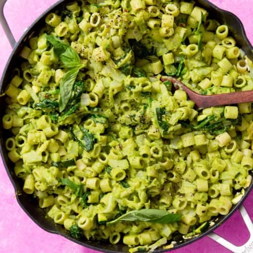 Green Goddess Pasta (using pasta that is shaped like small tubes) and greens in a large pan with a handle and a wooden spoon ready to serve.