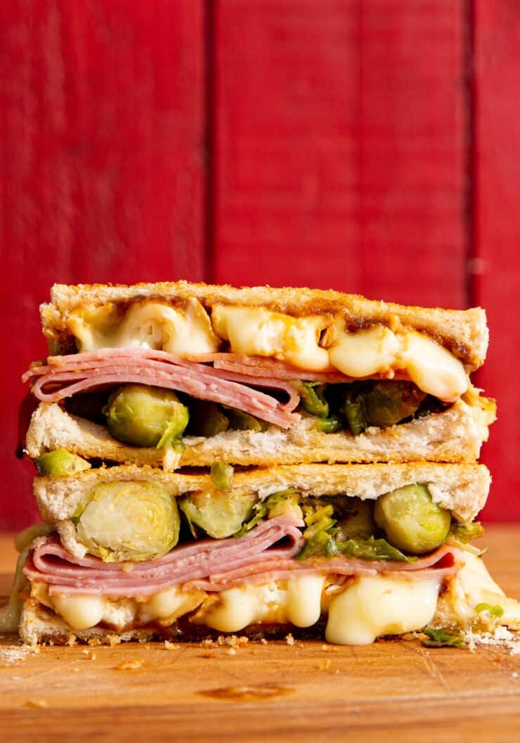 Ham and Camembert Toastie with layers of melted Camembert cheese oozing out, Brussel sprouts and slices of ham on 4 slices on white bread.