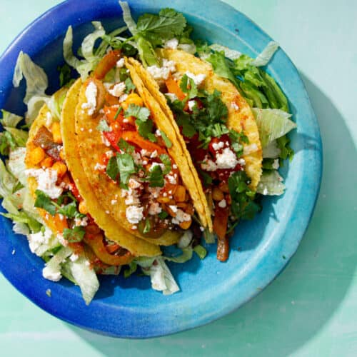 3 loaded Crunchy Veggie Tacos served on a plate with lettuce, chopped veg and crumbled feta.