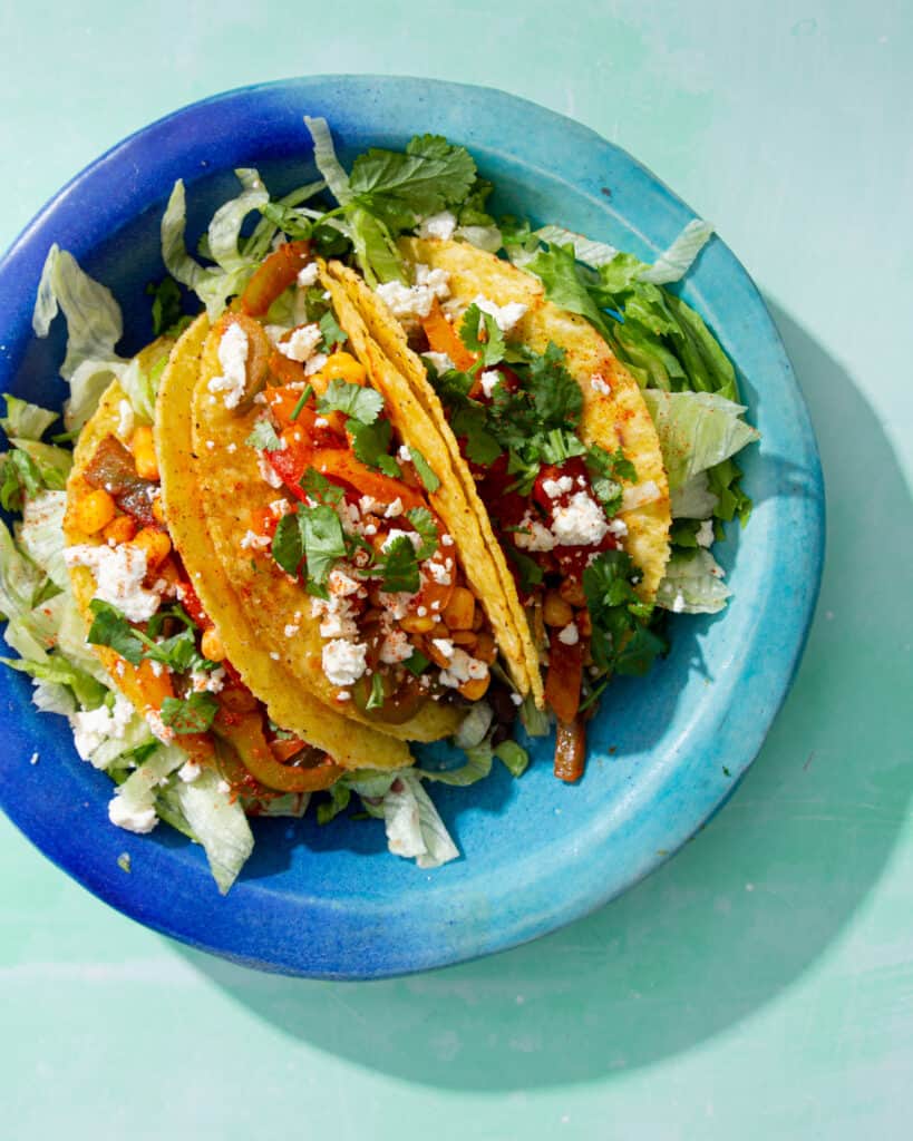 3 loaded Crunchy Veggie Tacos served on a plate with lettuce, chopped veg and crumbled feta.