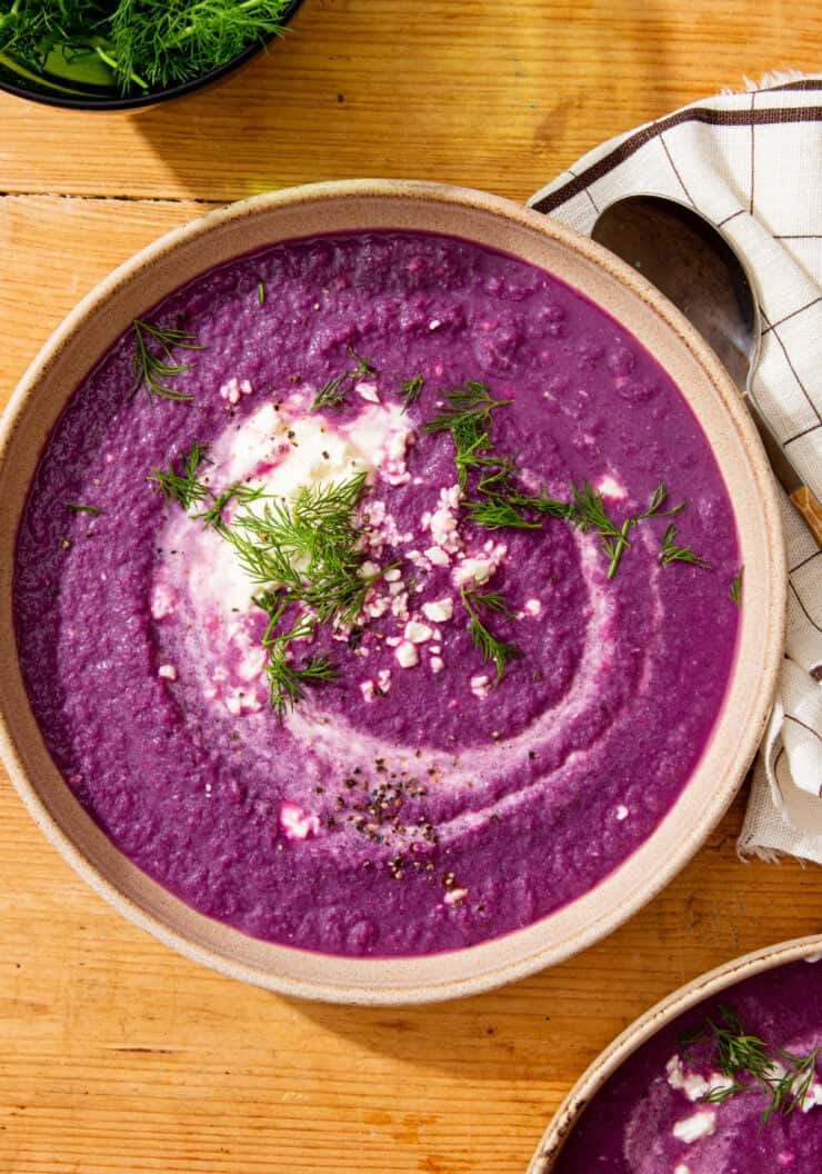 Red Cabbage and Feta Soup in 2 bowls with a serviette and spoon served with a sprinkle of feta, creme fraiche and some dill.