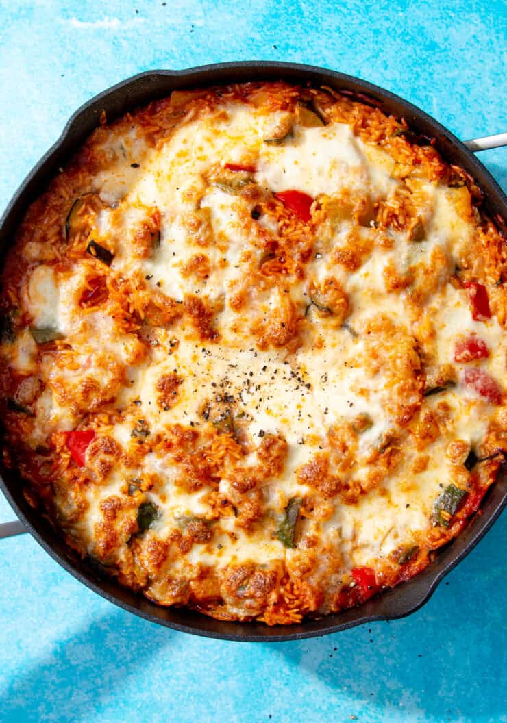 Cheesy Tomato Rice with melted mozzarella cheese, rice. loaded vegetables in a large pan on a blue background.