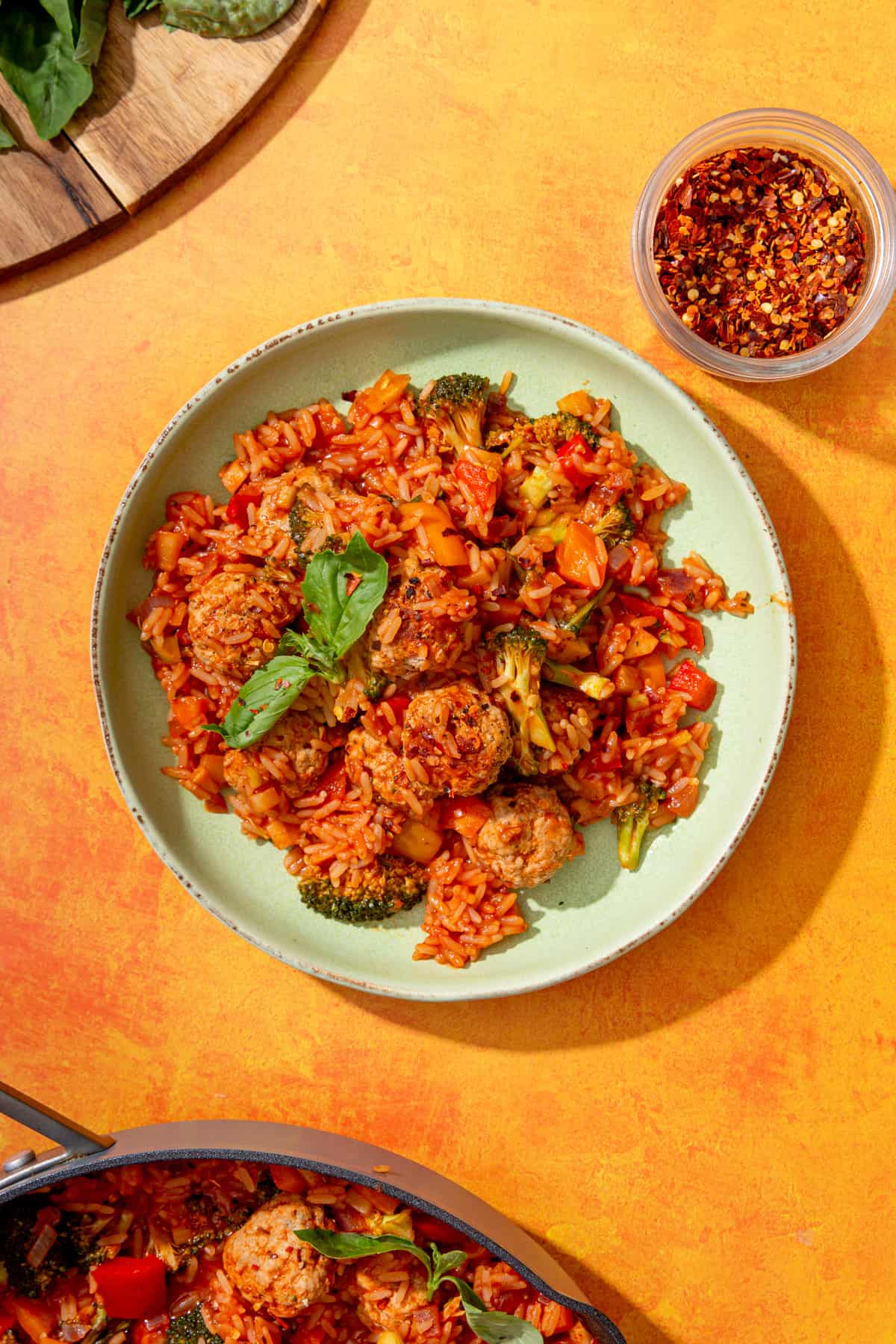 A bowl of meatballs and rice topped with basil on an orange background with fresh chillies.