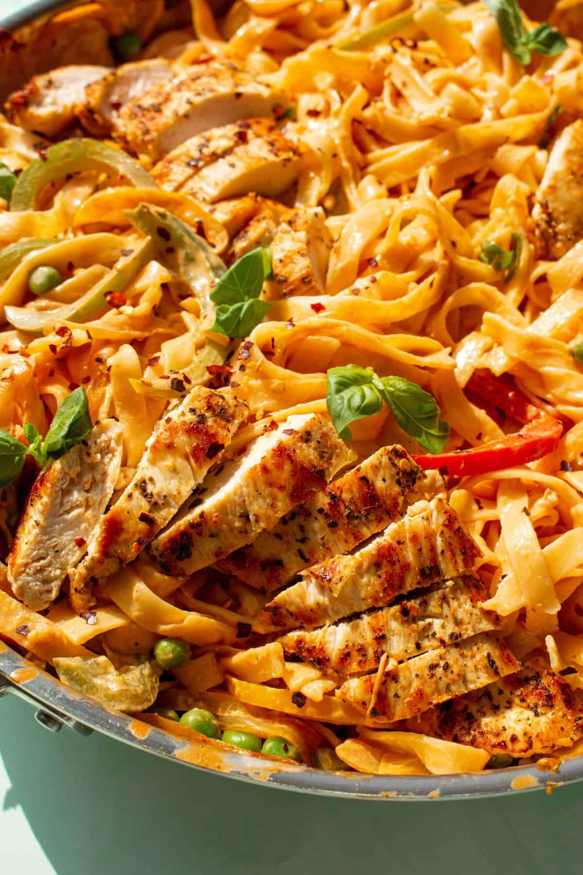 Close up view of Creamy Cajun Chicken Pasta with tagliatelle, chicken slices and topped with basil in a large stainless steel pan.