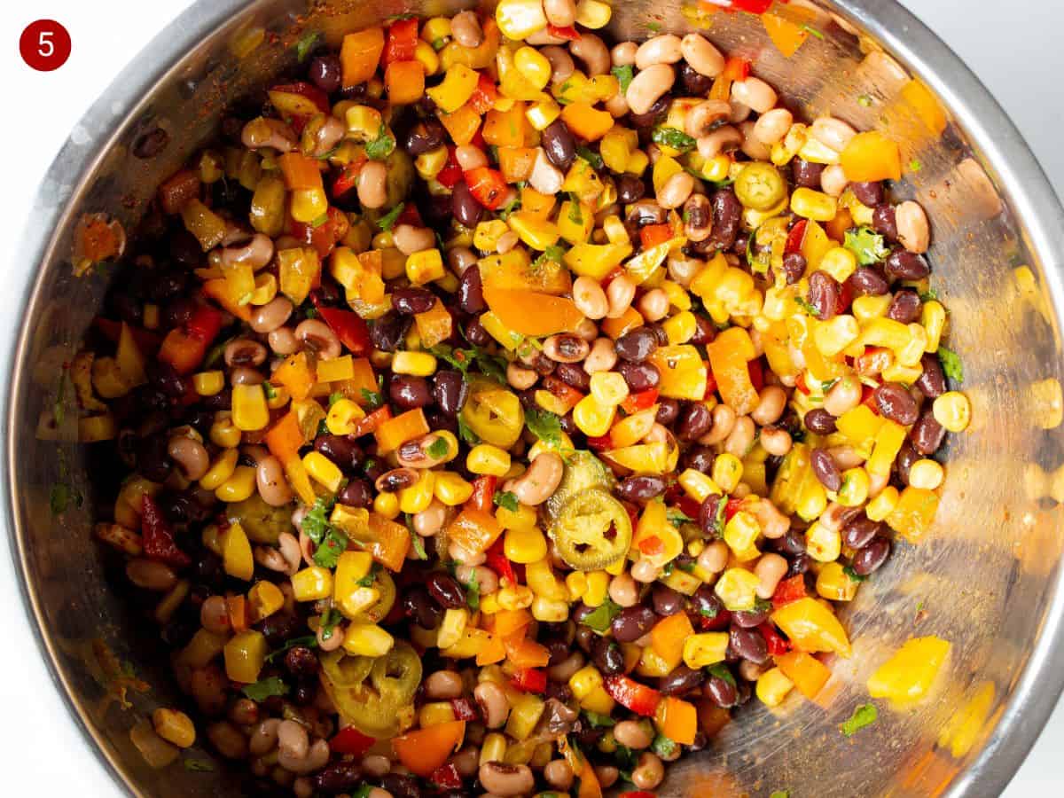 A large metal bowl with beans and finely sliced peppers, sweet corn and sliced jalapeno peppers.