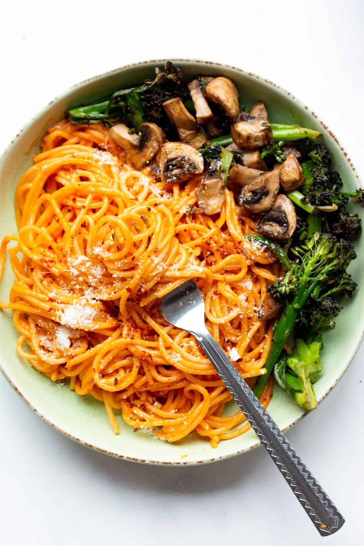 Tomatoey spaghetti in a bowl with a fork topped with grated parmesan and serve with mushrooms and broccoli.