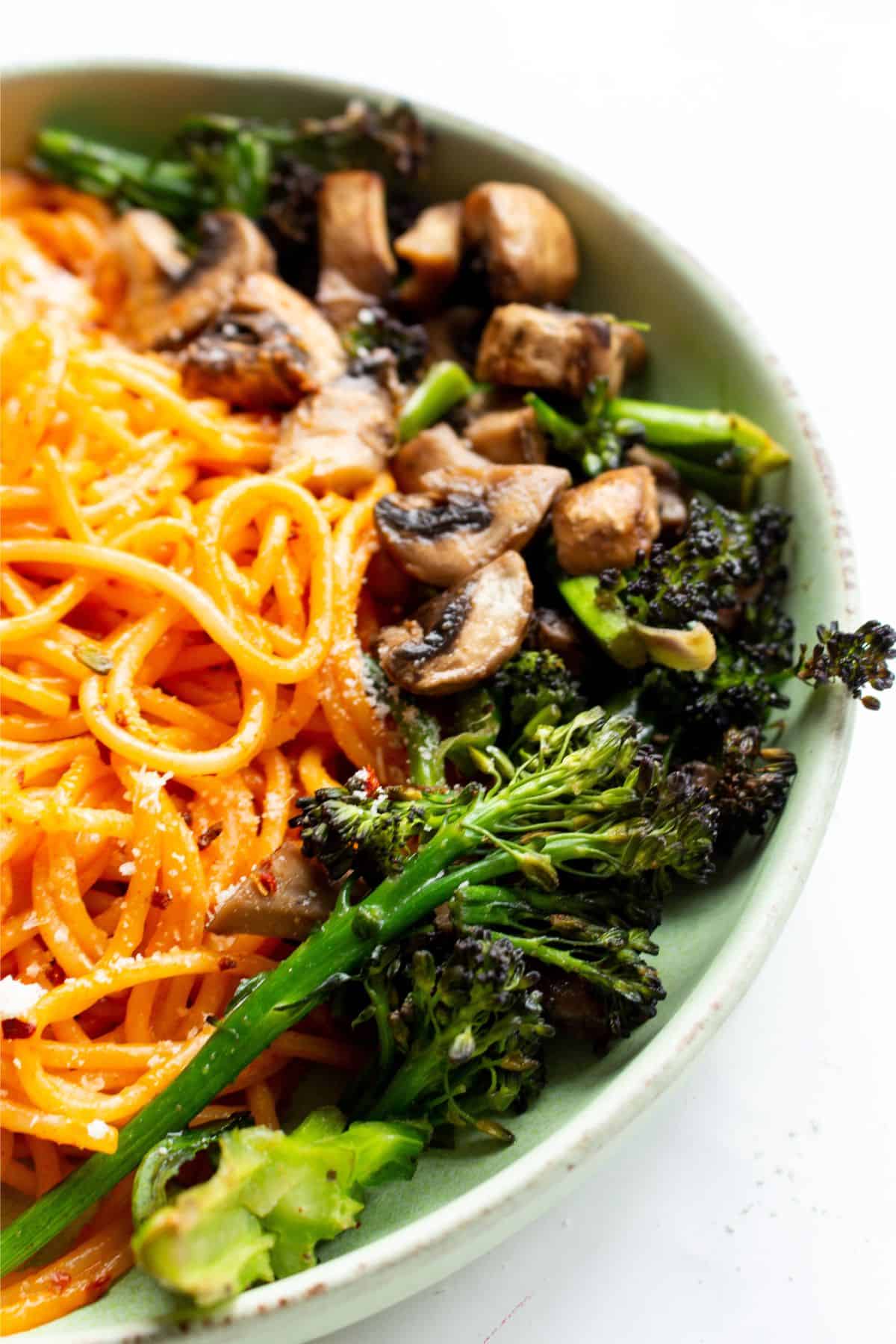 Half photo of bowl of spaghetti with mushrooms and broccoli on a green bowl on a white background.