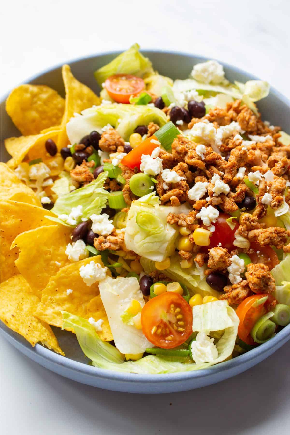 Close up of Dorito taco salad with browned mince, tomatoes, lettuce, Doritos and crumbled feta.