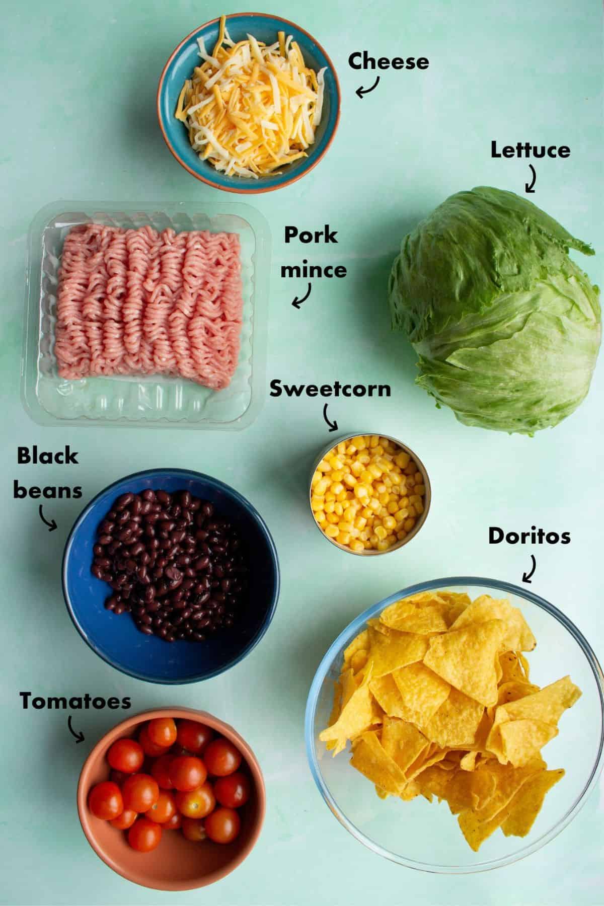 Ingredients to make the taco salad laid on a pale blue back ground and labelled.