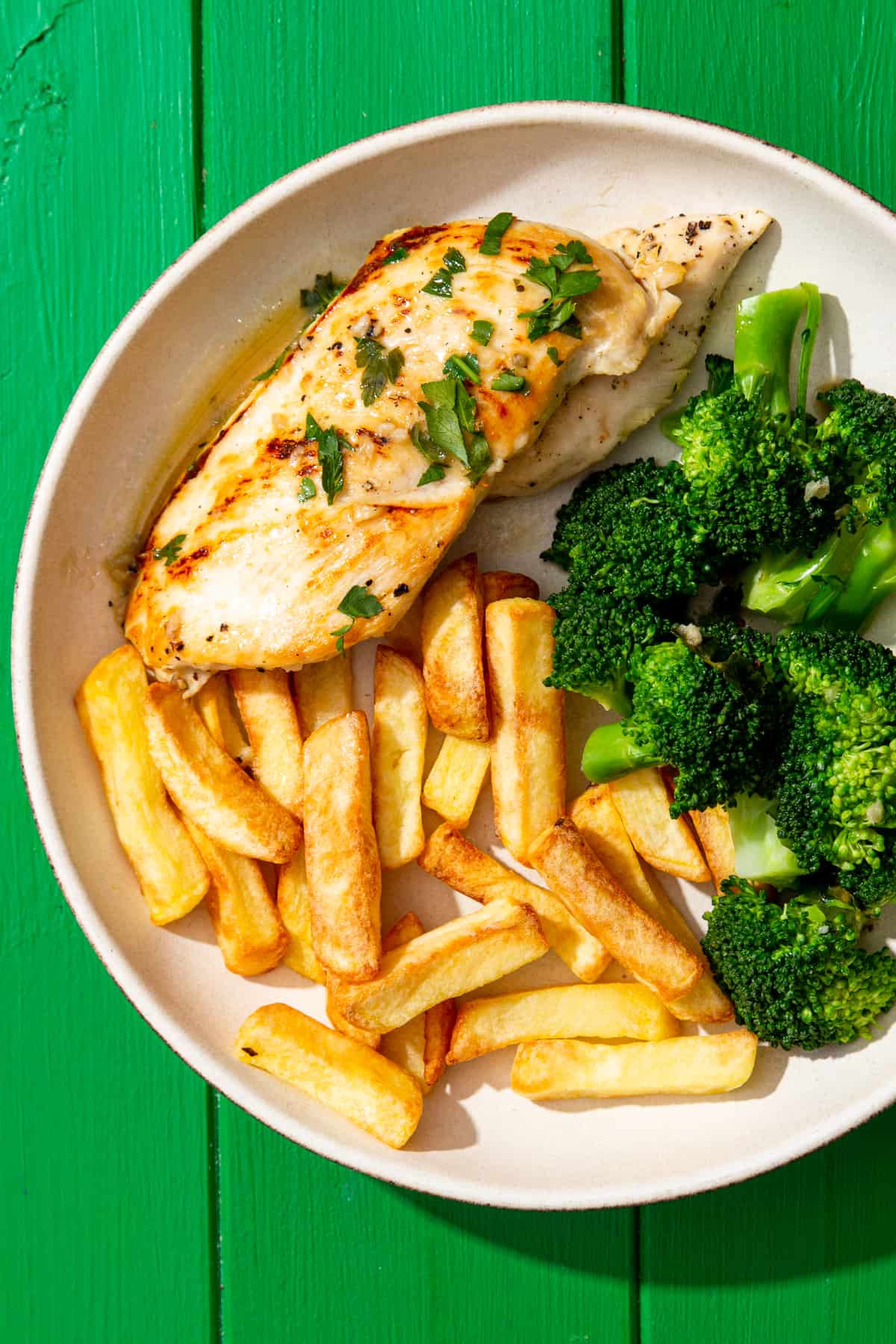 Golden browned chicken breast fillets with butter and parsley sauce  with fries and broccoli florets on a plate.