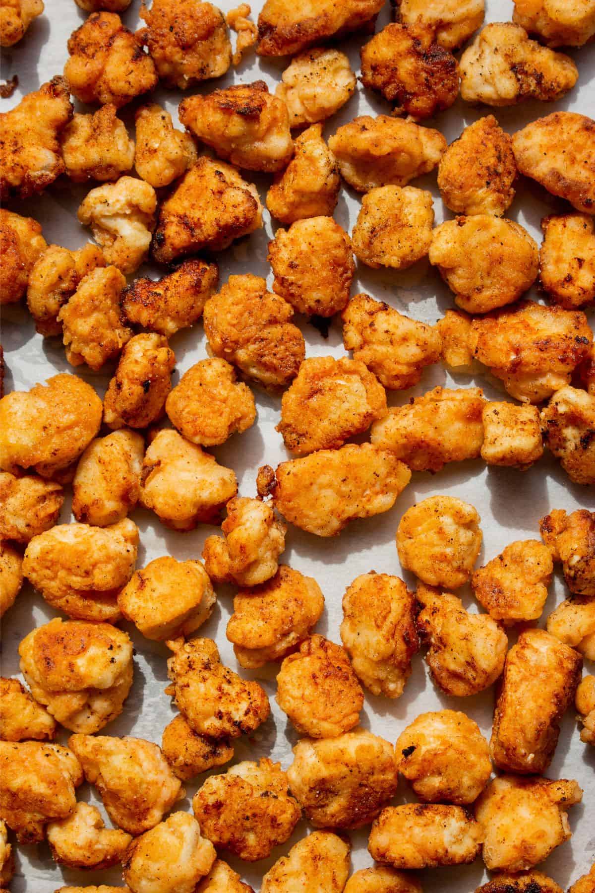 Close up of pieces of popcorn chicken pieces spread out over a stainless steel baking tray.