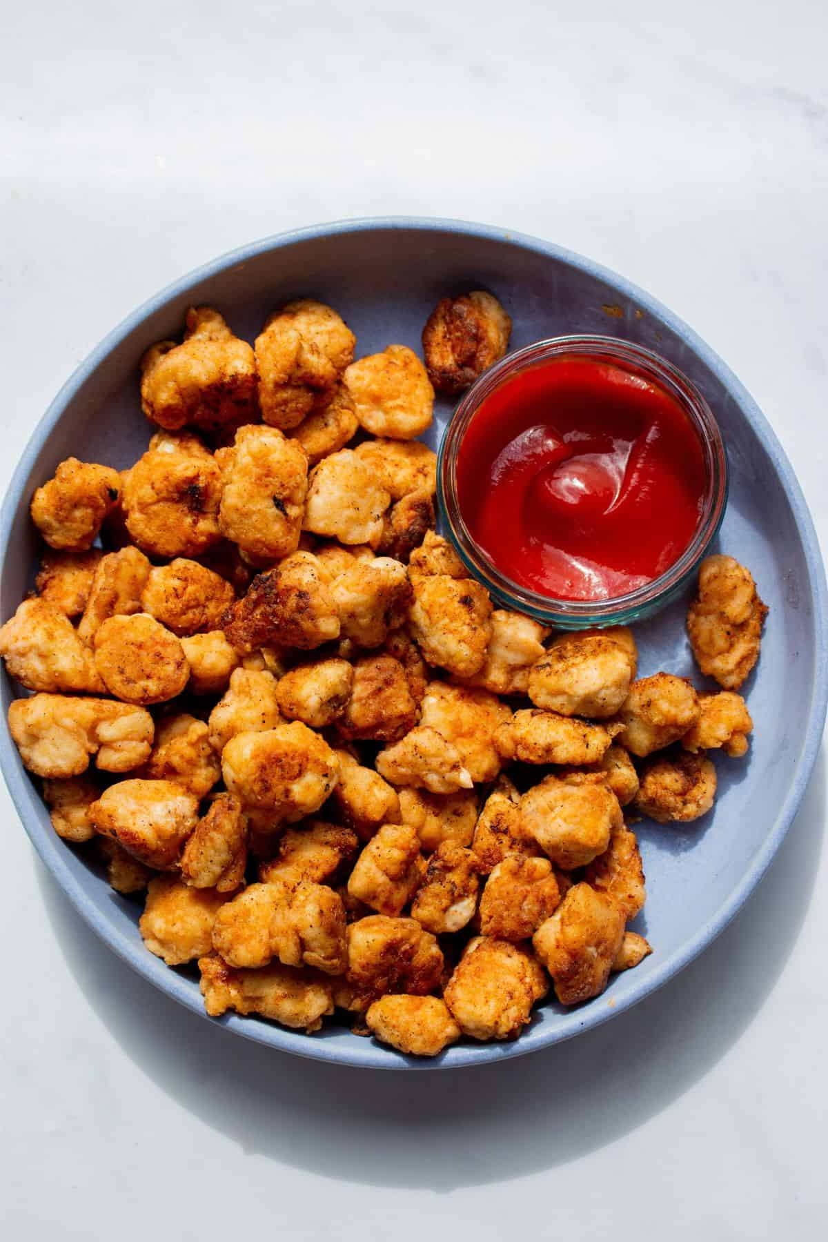 KFC pop corn chicken pieces served in a blue dish with tomato ketchup in a smaller glass dish on same plate.