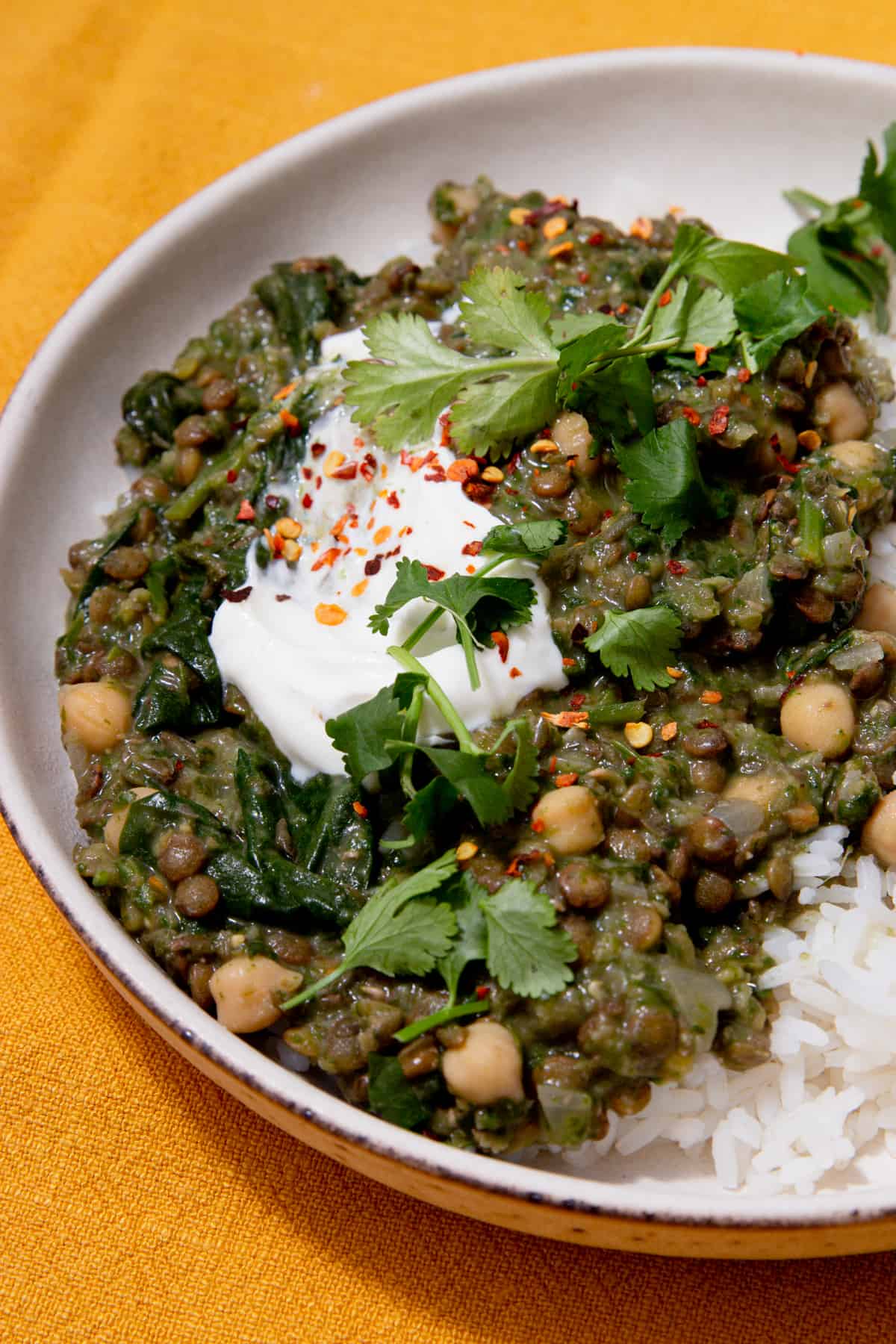 Close up of lentil curry with chickpeas and spinach topped with chilli flakes, yogurt and coriander.