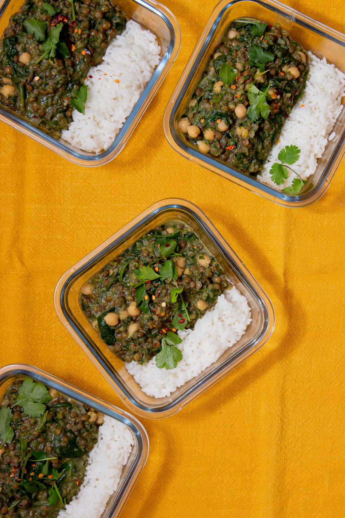 Lentil and spinach in 4 square glass meal prep containers with white rice, chickpeas and coriander.