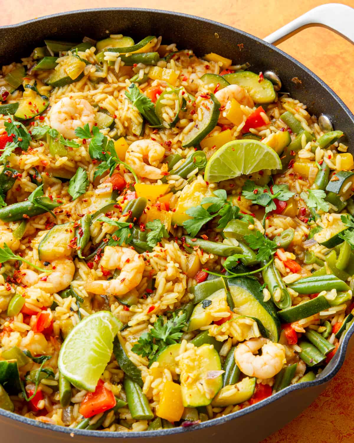 Close up of rice with vegetables, large prawns, rice and garnished with fresh parsley and lime in a large pan