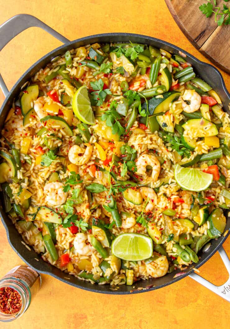 Prawns, rice and vegetables in a large pan topped with lime wedges and parsley.