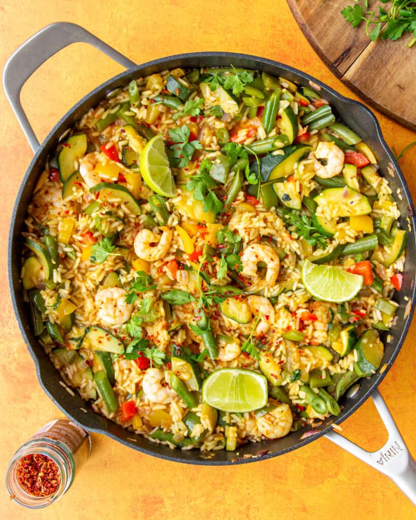 Prawns, rice and vegetables in a large pan topped with lime wedges and parsley.
