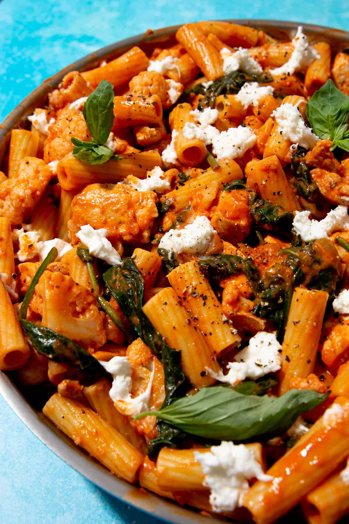 Close up of pasta with tomatoey sauce and topped with pieces of mozzarella and basil.