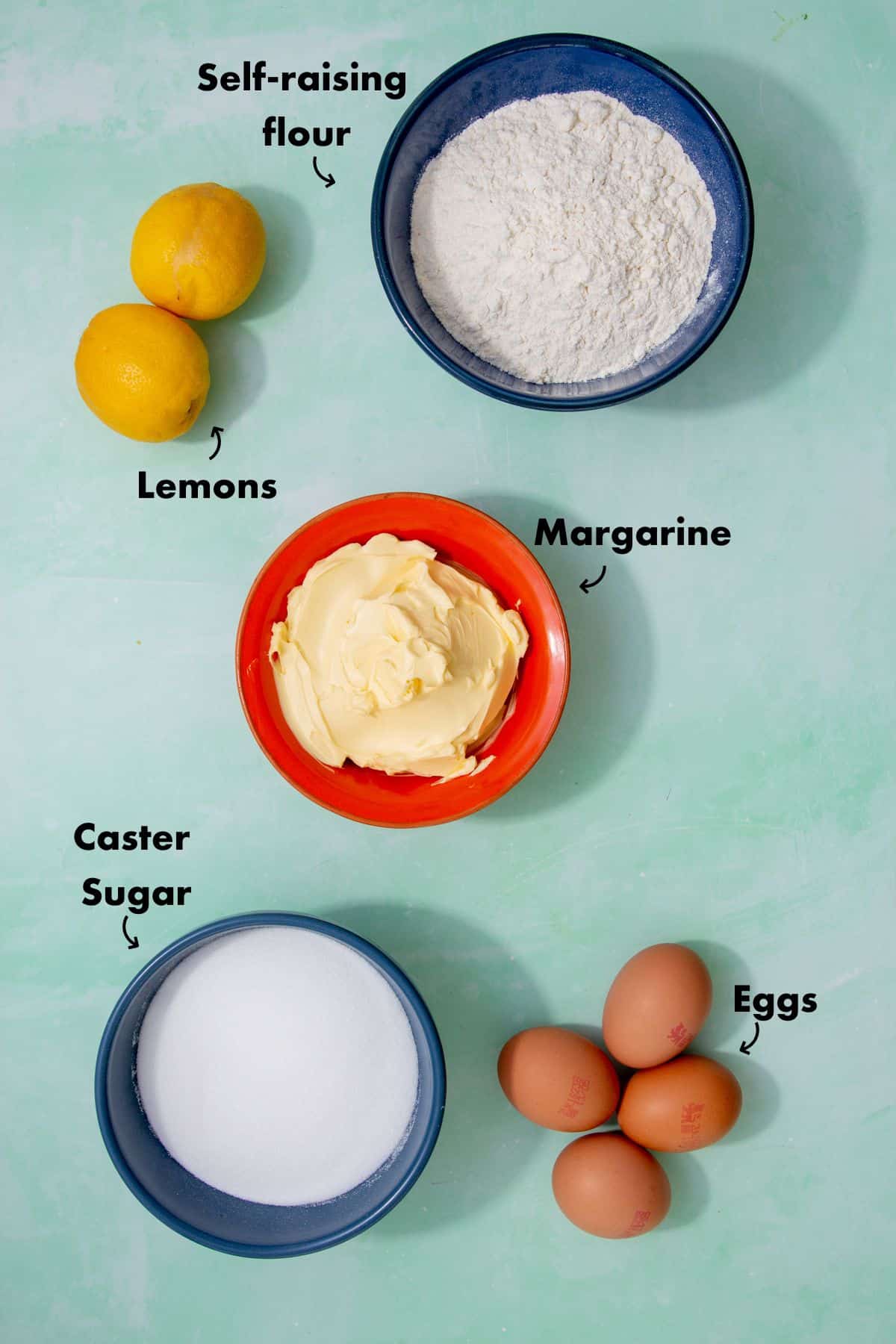 Ingredients for lemon cake laid out on a pale blue background and labelled.