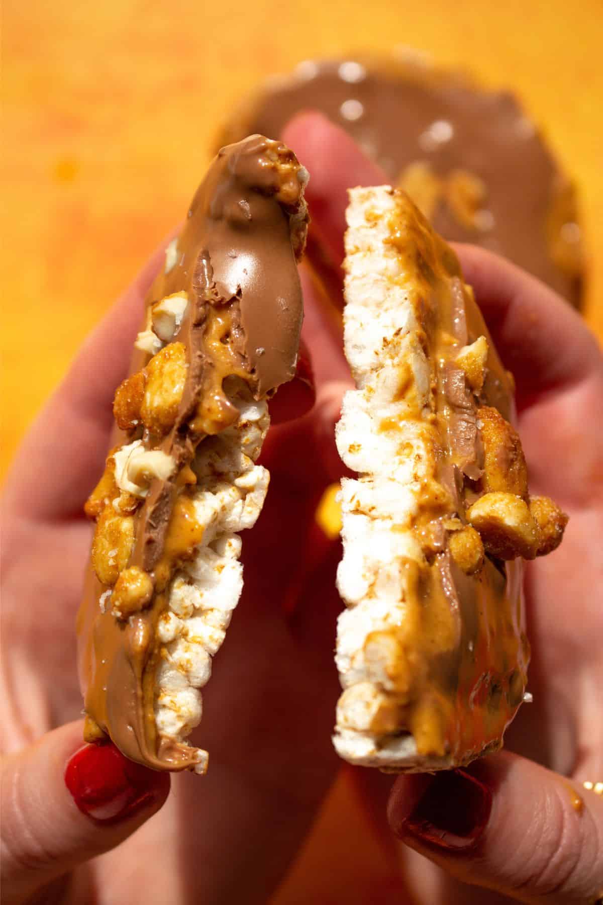 Rice cake broken in half and held with 2 hands to show the chocolate and peanut butter filling.