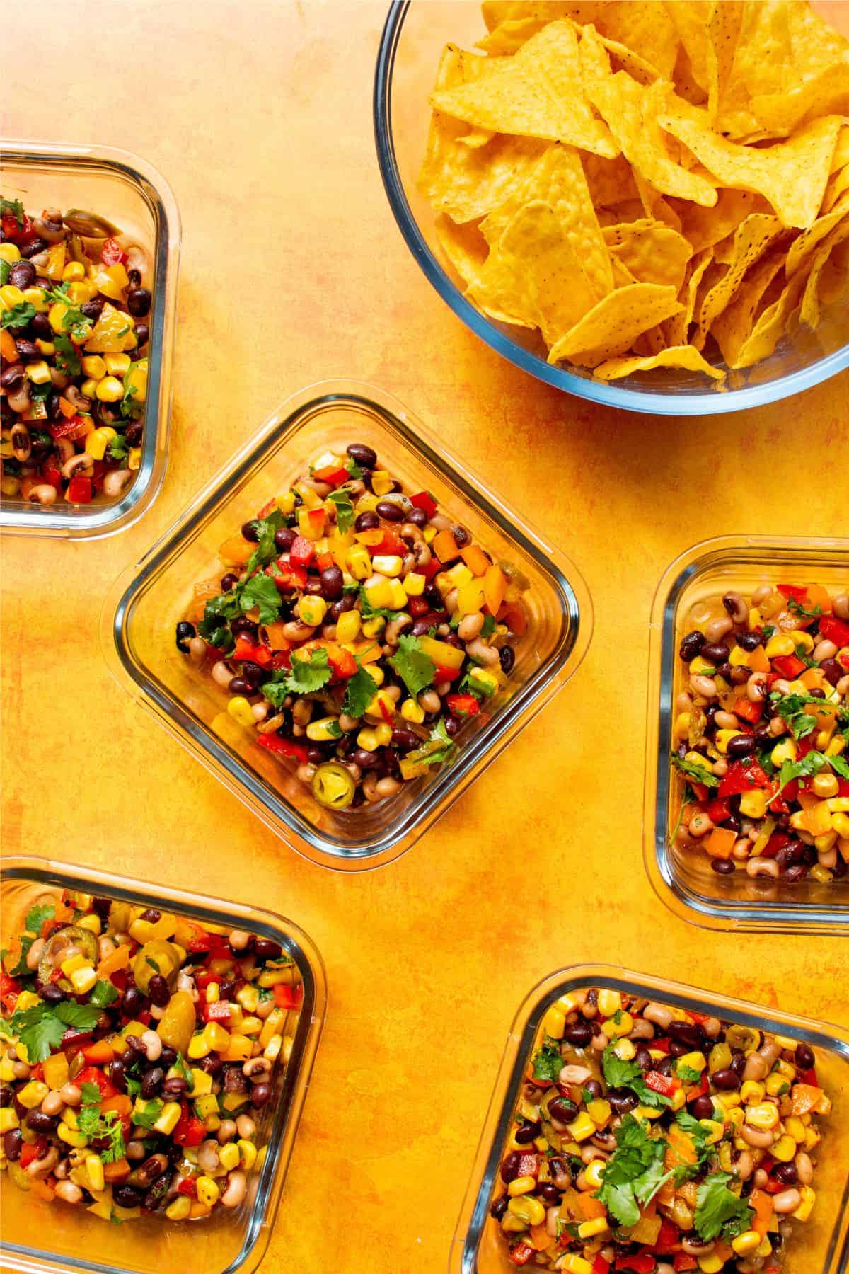 Mixed bean salad served in 3 square glass meal prep containers with a large bowl of tortilla chips.