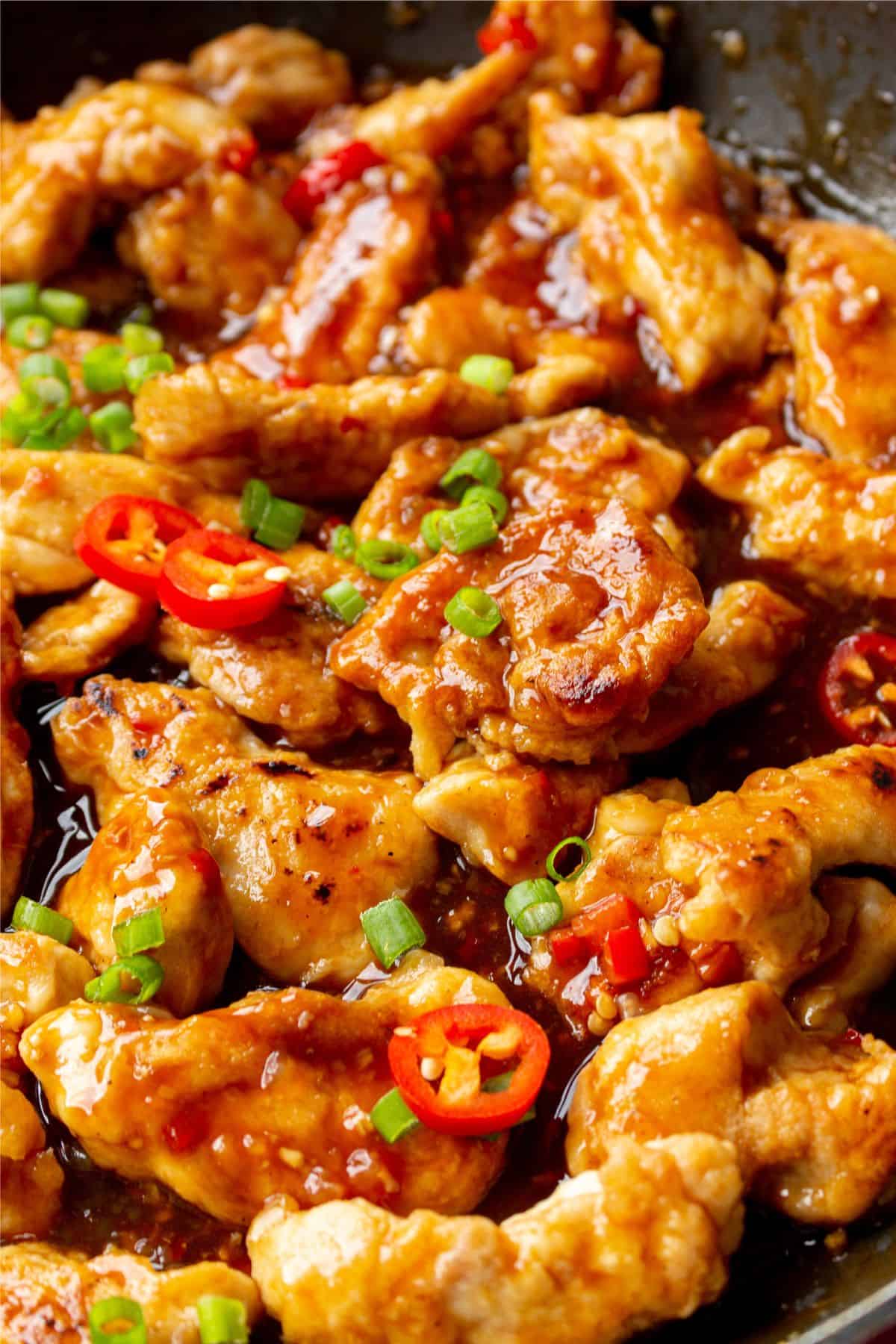 Close up of Crispy Chicken topped with sliced spring onion and red chillies in a pan.