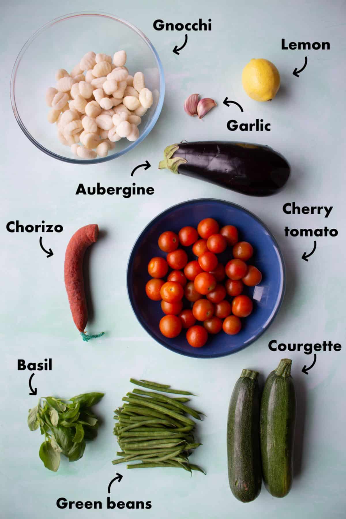 Ingredients to make the gnocchi with roasted vegetables laid out on a pale blue background and labelled.