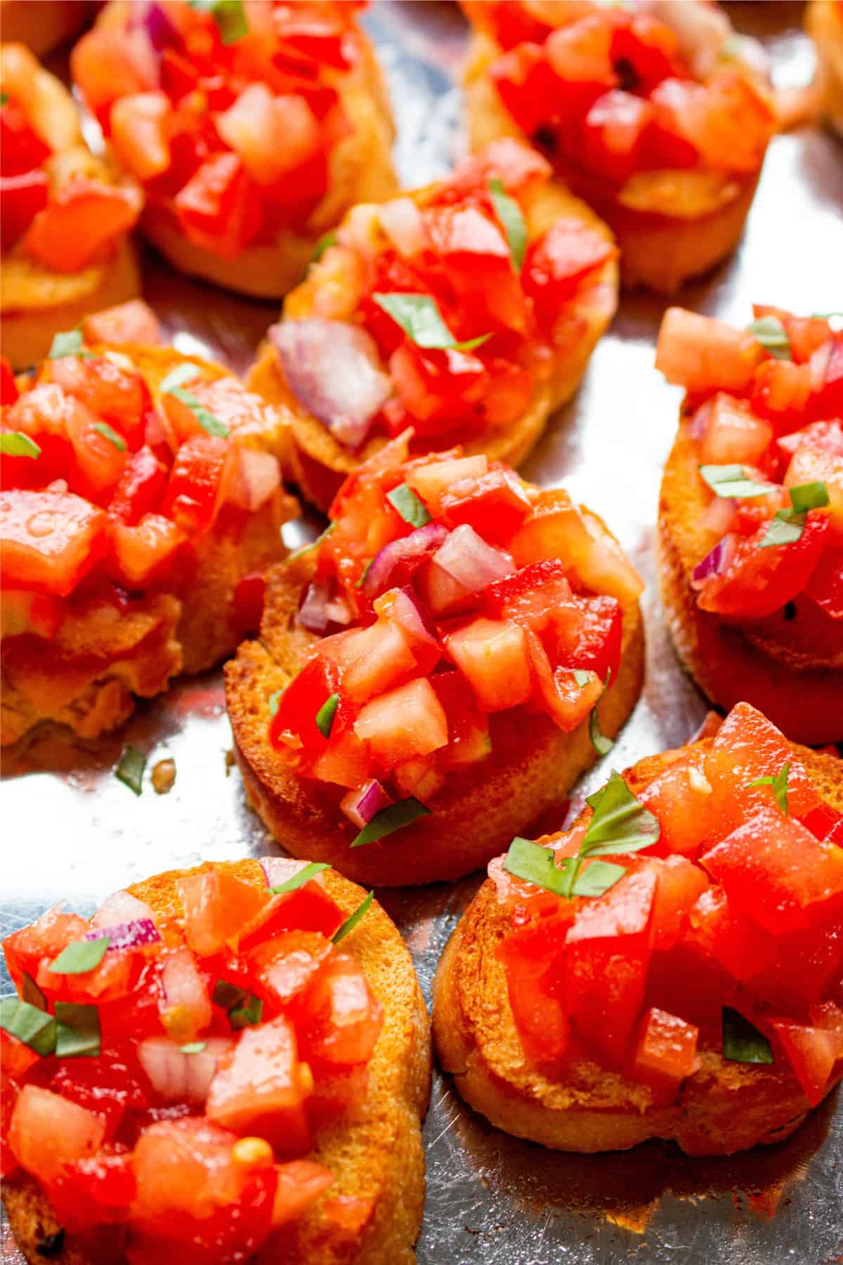 Close up of small rounds of toasted bread topped with chopped tomatoes and onions on a baking tray.