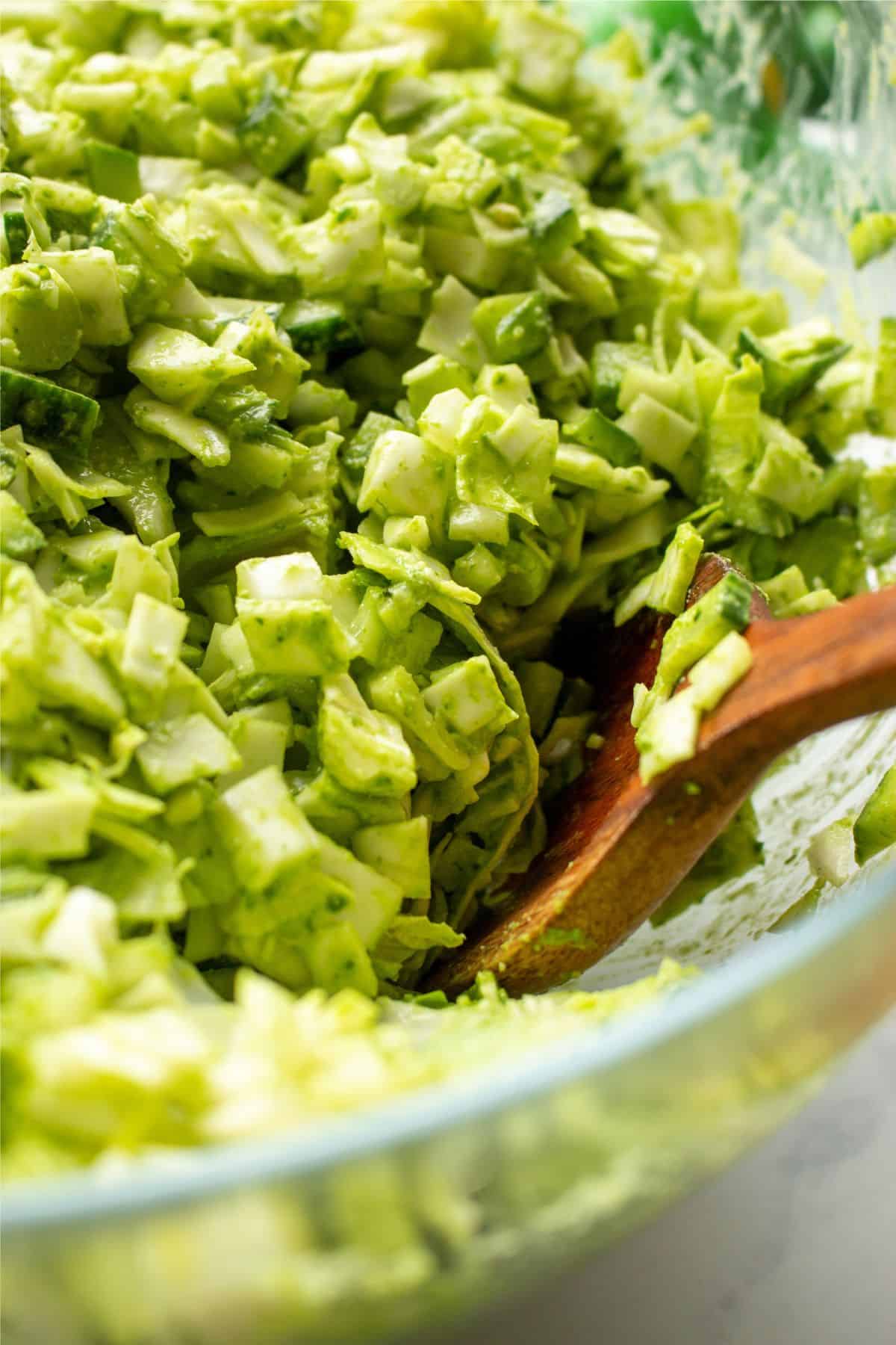 Close up of chopped salad in a large glass bowl with dressed and stirred with a wooden spoon.