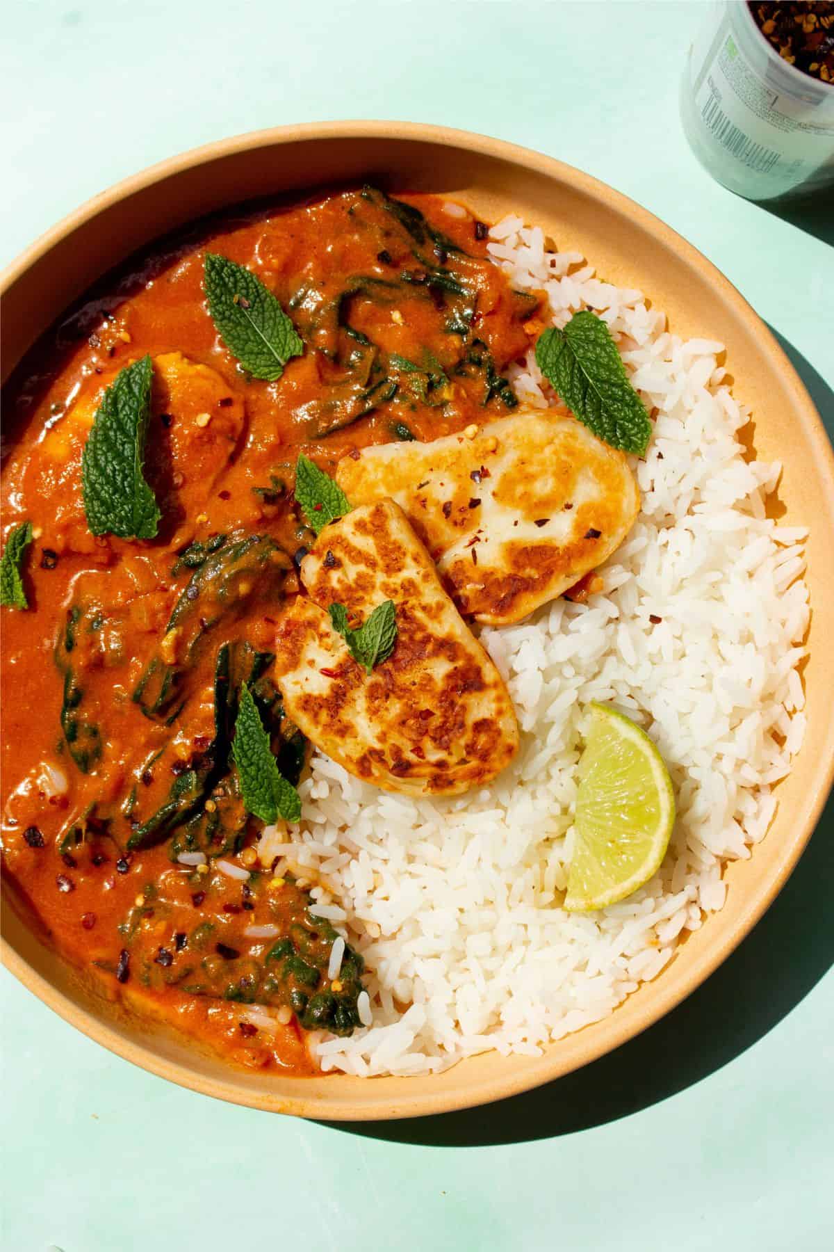 Curry served on a plate with rice and topped with fresh mint, lime and golden browned halloumi.