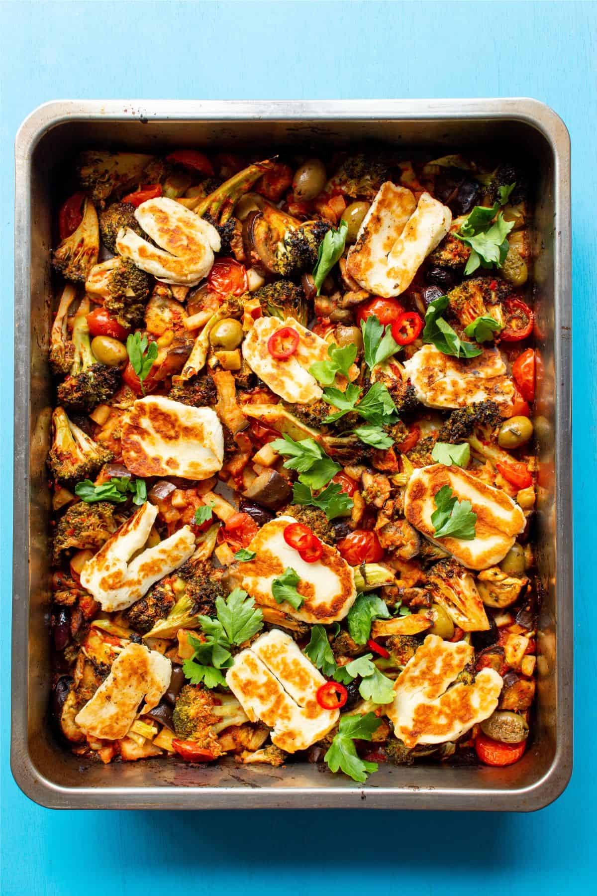 Roasted vegetables with olives and parsley, red chilli slices and golden bowned in halloumi in a baking tray.