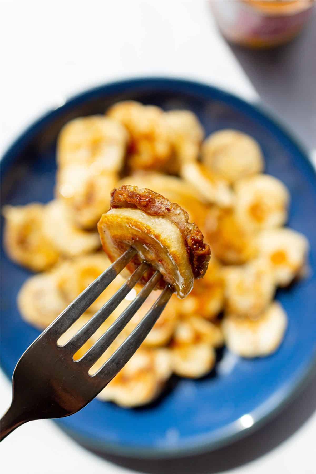 Close up of a metal fork with a mini pancake with banana and Biscoff with the blue plate of pancakes faded in the background.