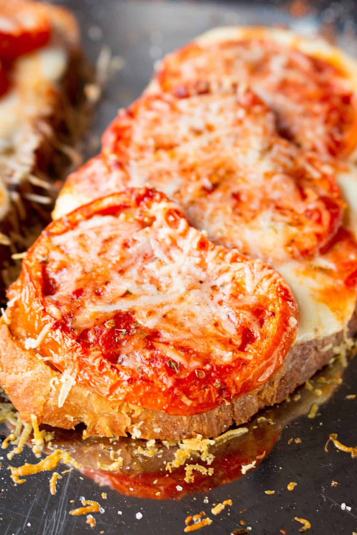 Close up of pizza toast with tomatoes, melted mozzarella and parmesan.