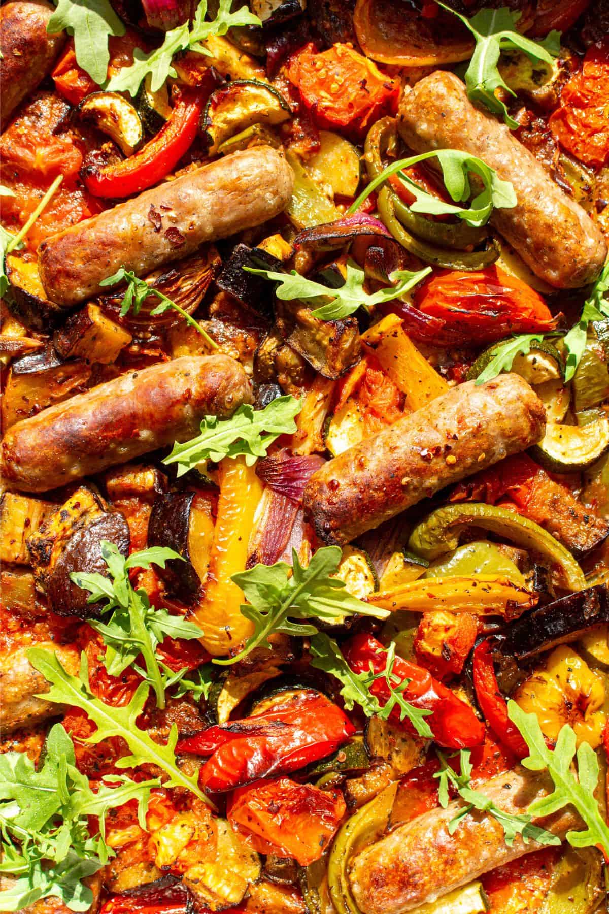close up of roasted sausages and vegetables (peppers, courgettes, red onion and courgettes) in stainless steel baking tray.