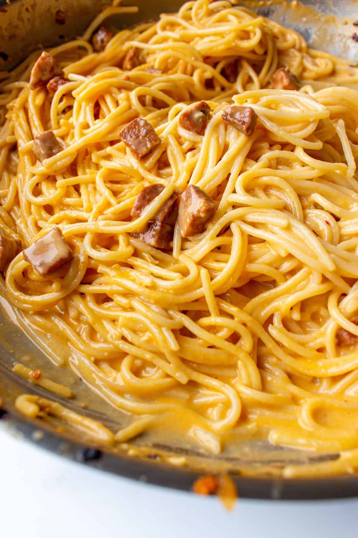 Close up of carbonara with spaghetti, small slices of chorizo and the eggy carbonara sauce in a large stainless steel. 