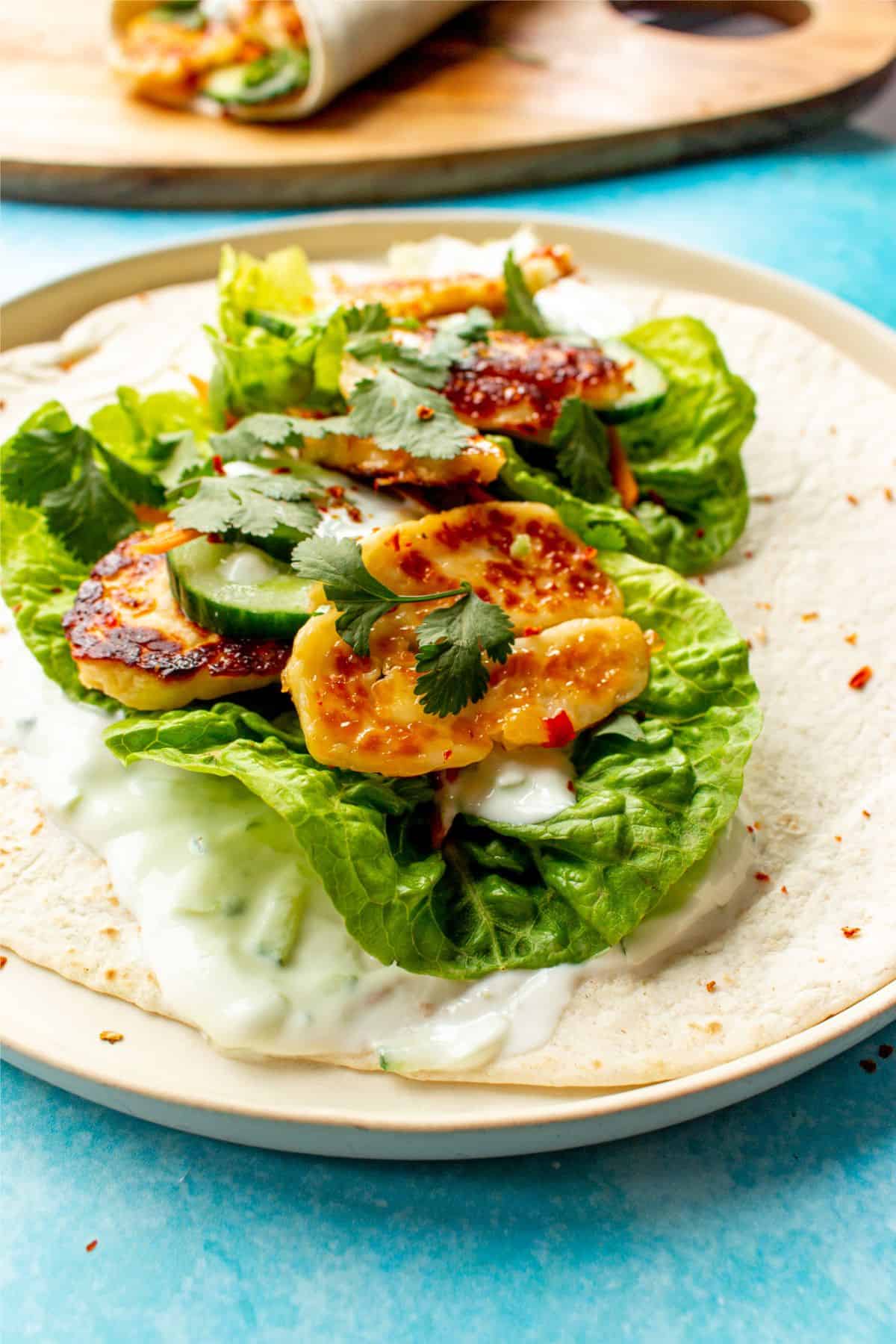 Close up of a halloumi wrap on a plate with lettuce, carrot, halloumi and topped with the sweet chilli and Greek yogurt.