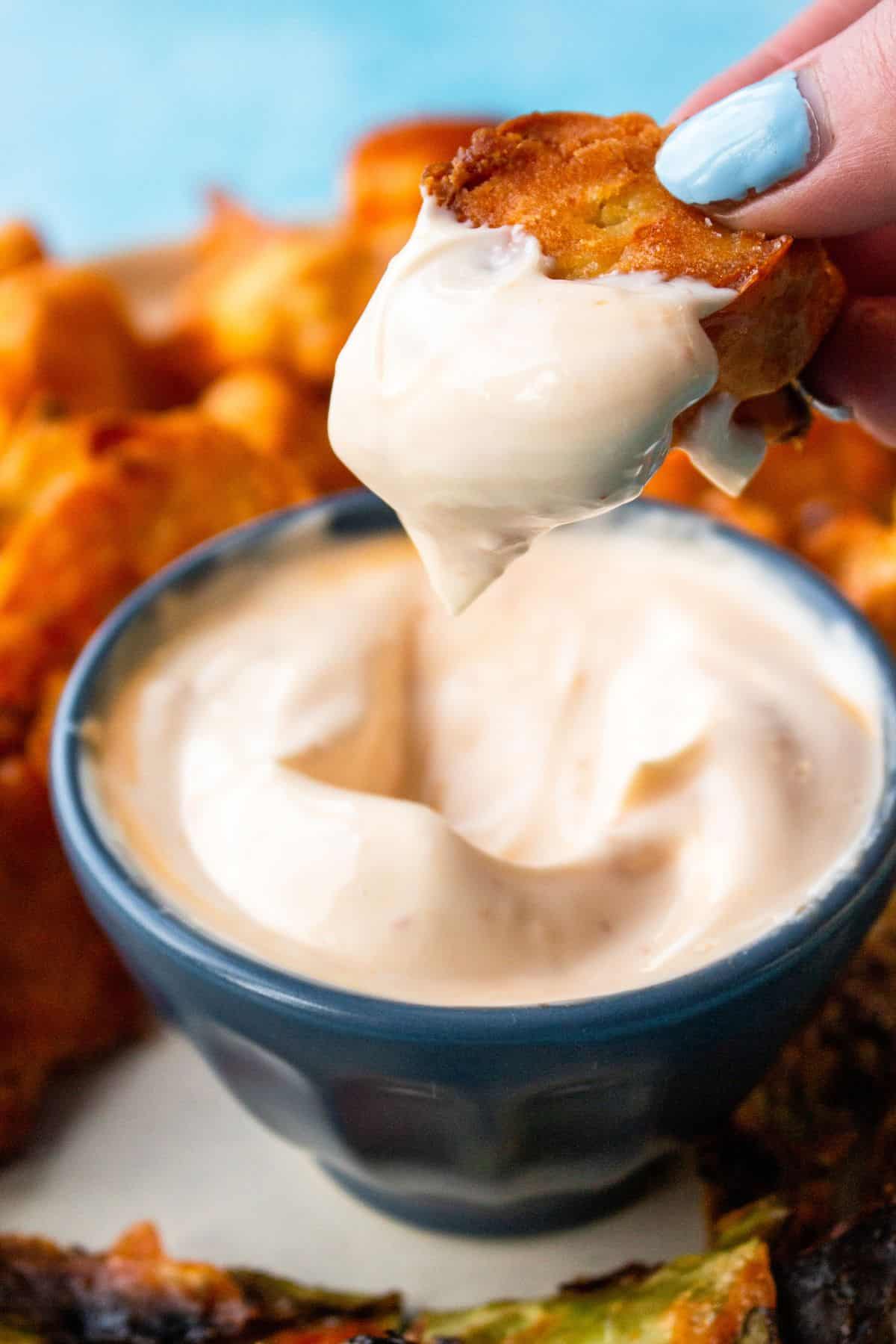 Close up of a piece of crispy cauliflower being dipped into the chill mayo.