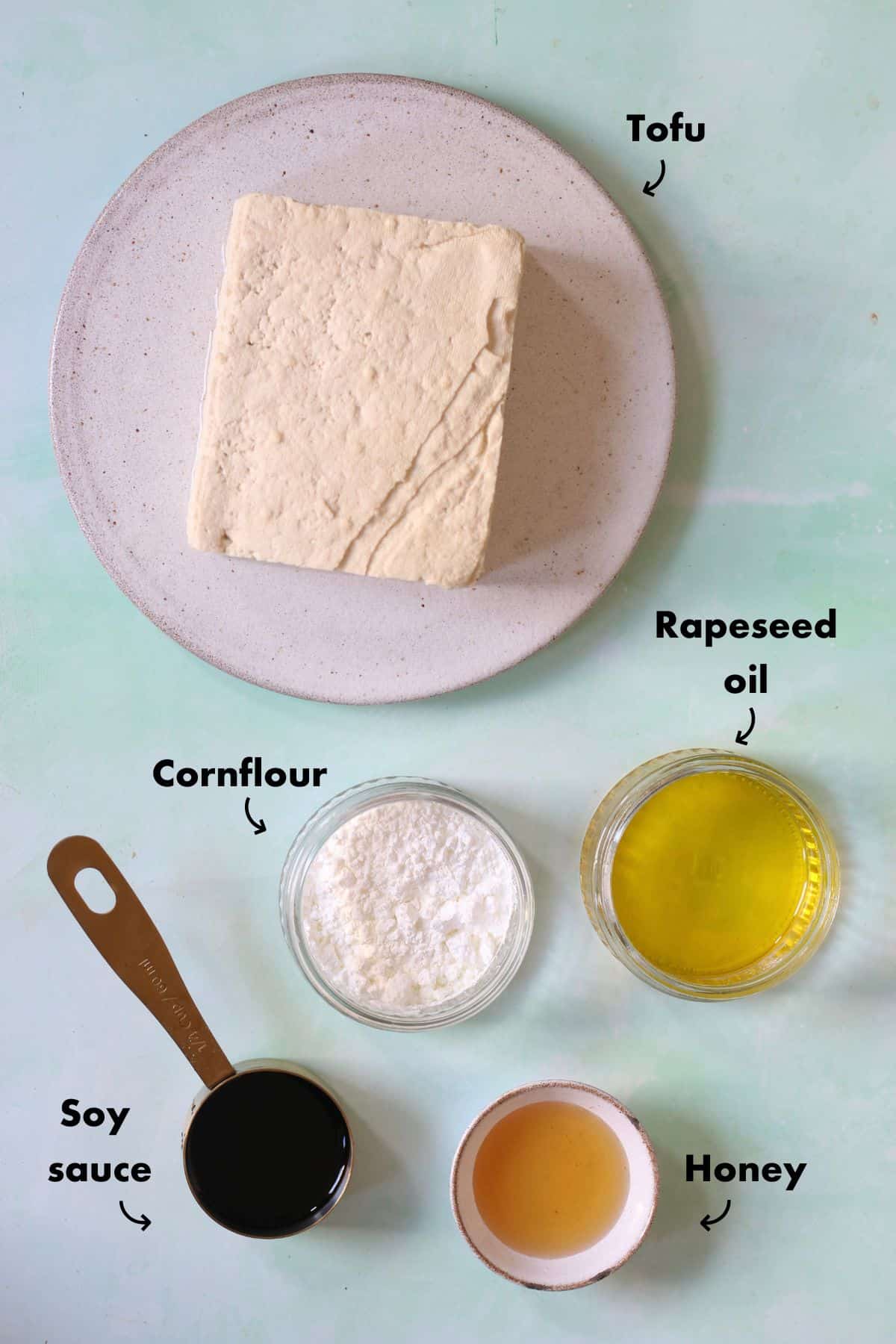 Overhead shot of ingredients to make crispy tofu laid out on a plae blue background and labelled.