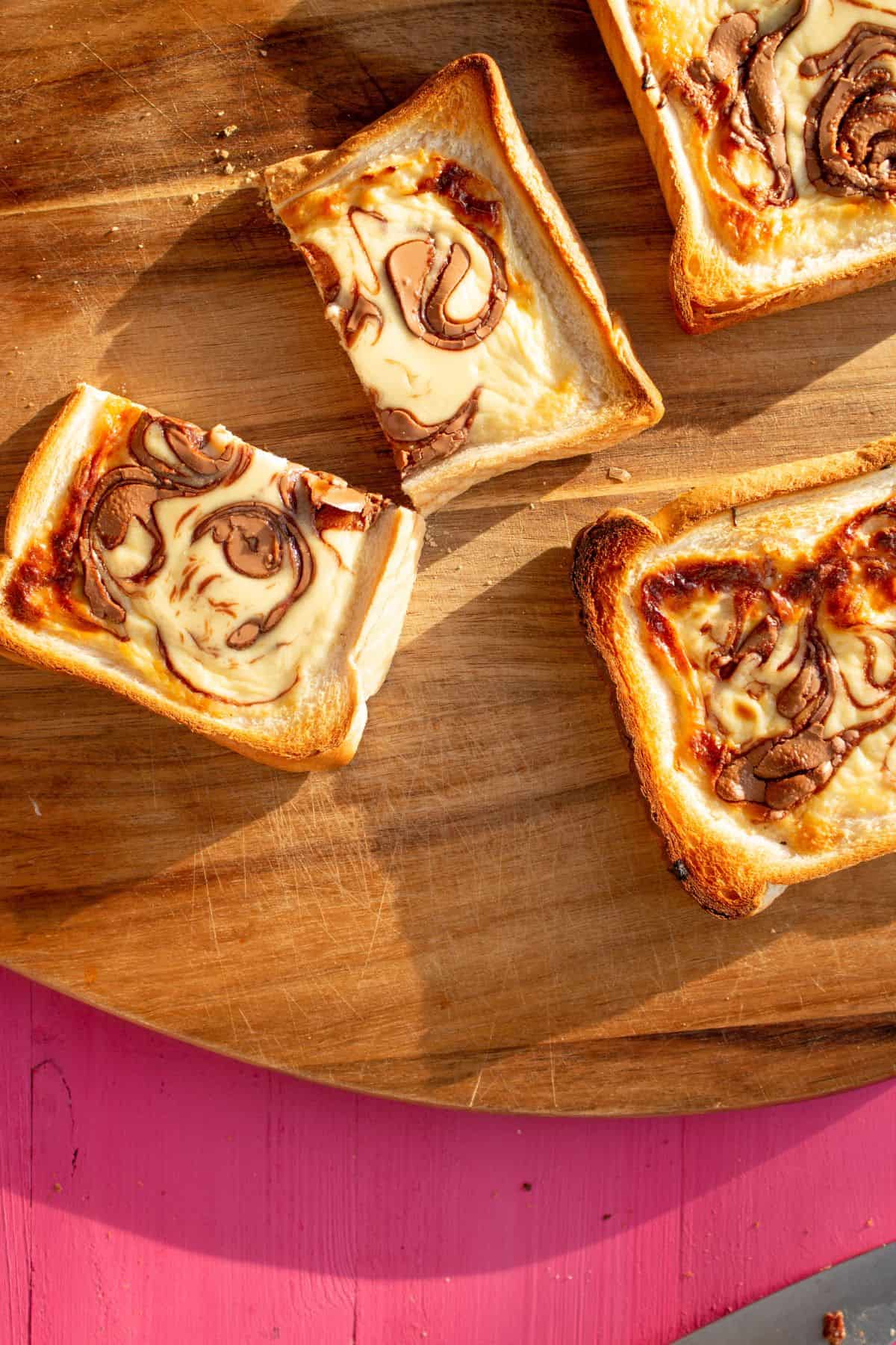 Chocolate custard toast sliced in halves on a chopping board on a pink background.