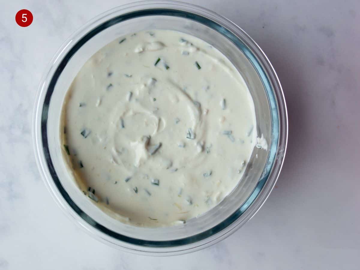 A round glass bowl with cream cheese with pieces of chives.