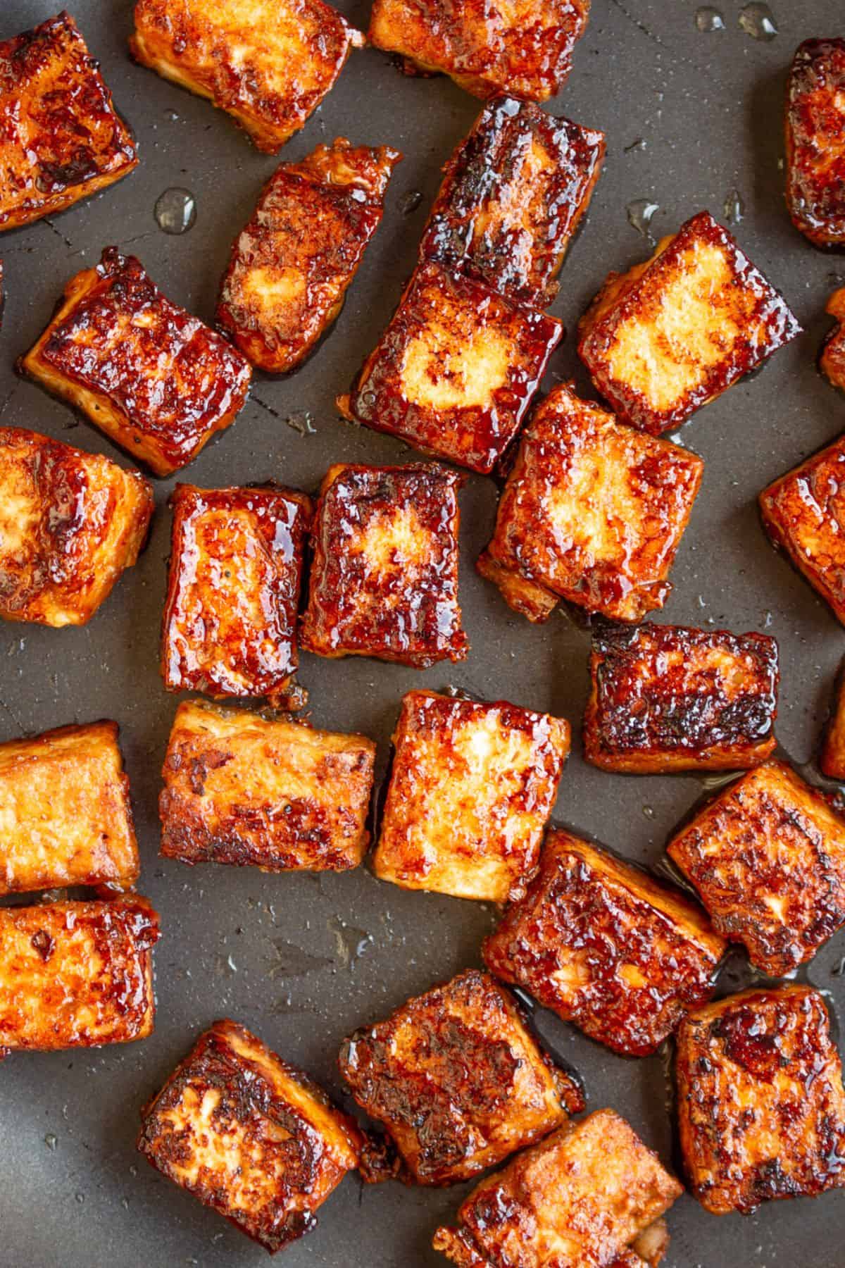 Close up of lots of browned and crispy tofu cubes/rectangles in a pan.